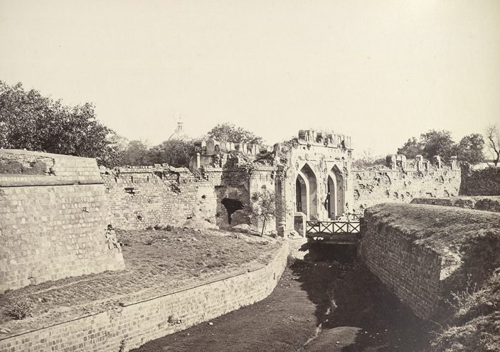 An old stone gateway with its walls pitted and broken by shellfire, in an old black-and-white photograph