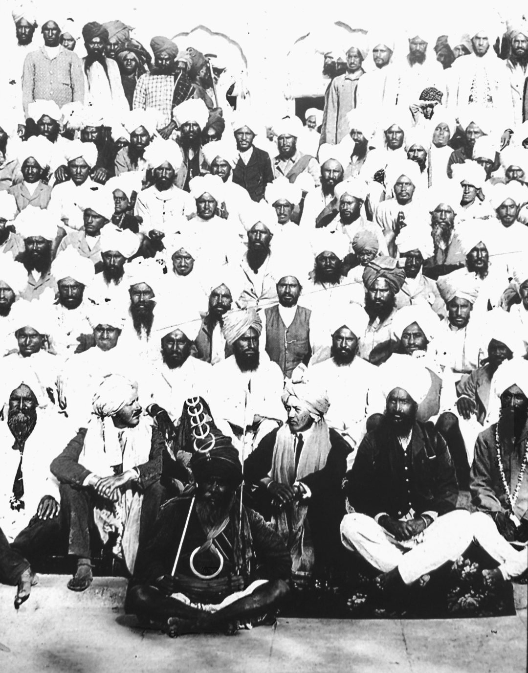 An old group photograph of turbaned Sikh men, some holding spears, standing with two men in European dress in front of a shrine
