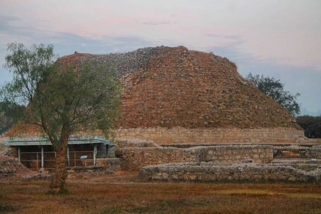 The ruined round mound of a large Buddhist stupa surrounded by low stone walls and the bases of smaller stupas
