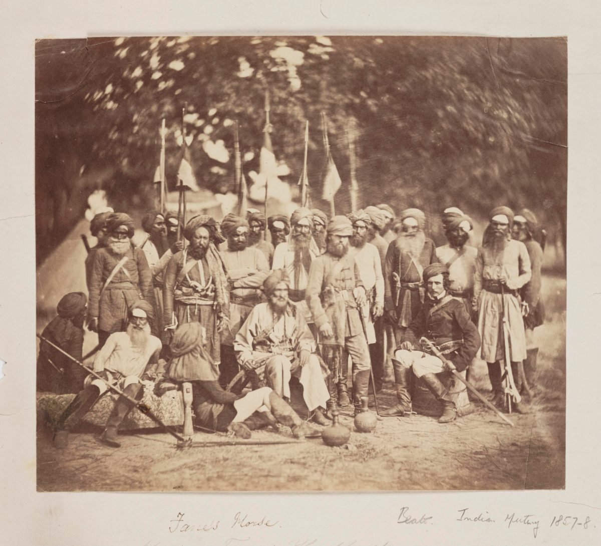 A group of turbaned cavalrymen in long coats posing with two British officers in an old photograph