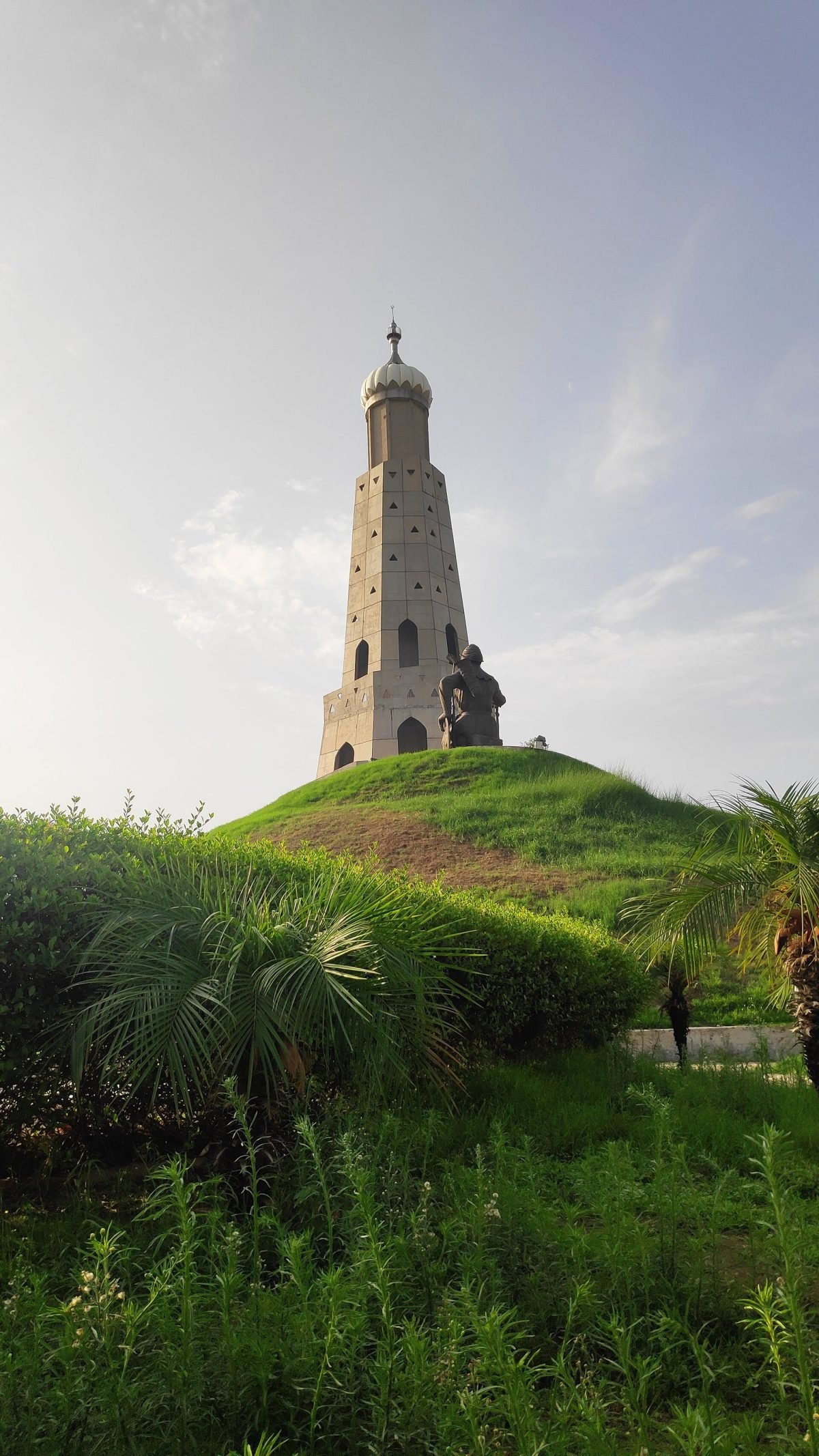 A tall pale victory tower beside a statue of a horseman, at the memorial at Chappar Chiri