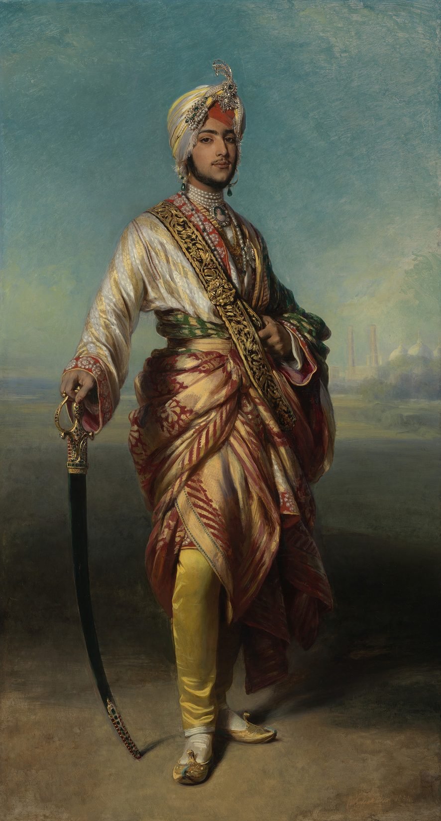 A full-length oil portrait of a young man in a jewelled turban and richly embroidered robes, standing with one hand on a sword