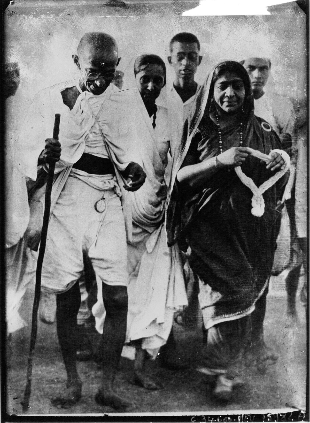 Gandhi, with shaved head and white cloth, sitting beside Sarojini Naidu, a woman in a dark sari, both looking down