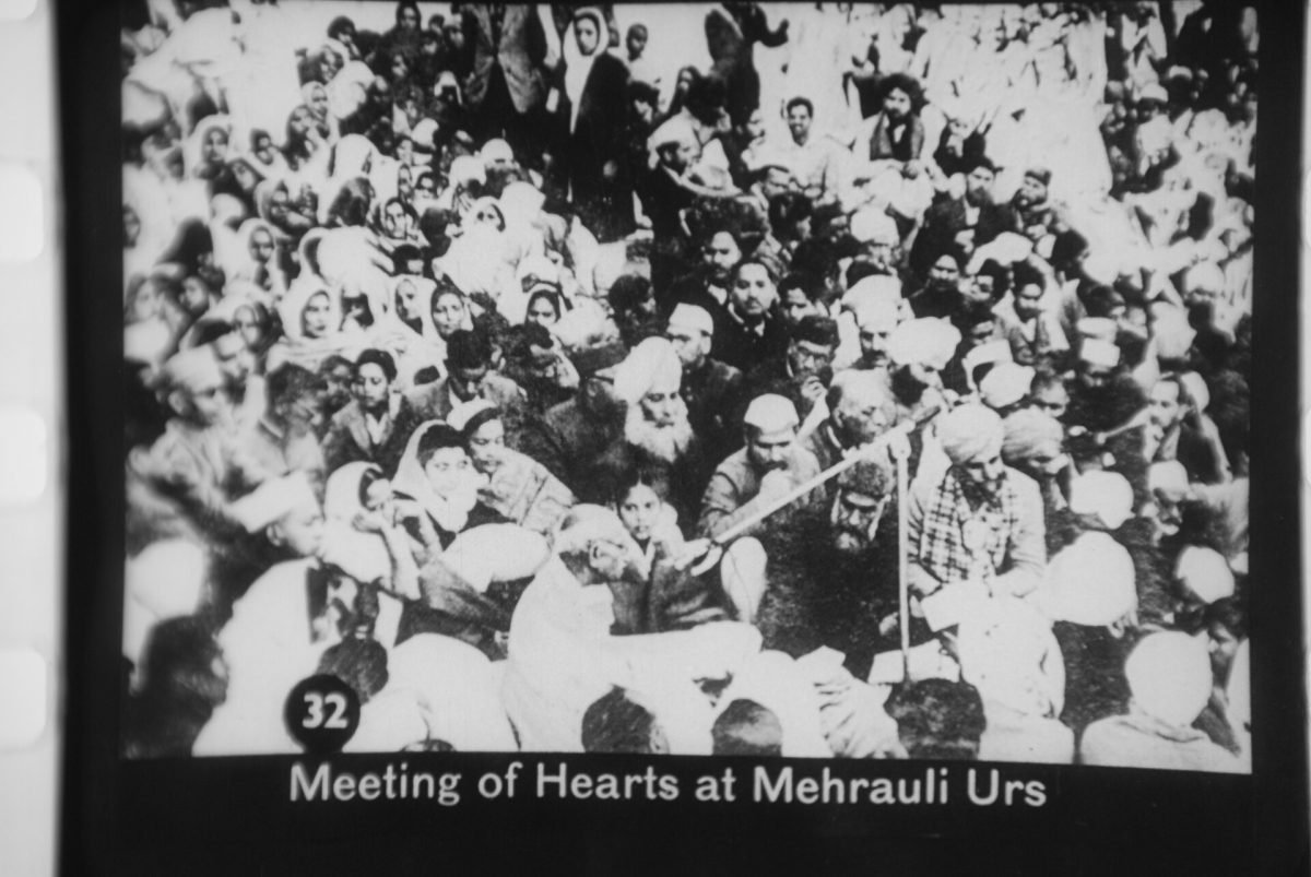 Black and white photograph of Gandhi, bare-chested with a shawl, among a crowd of men at a shrine