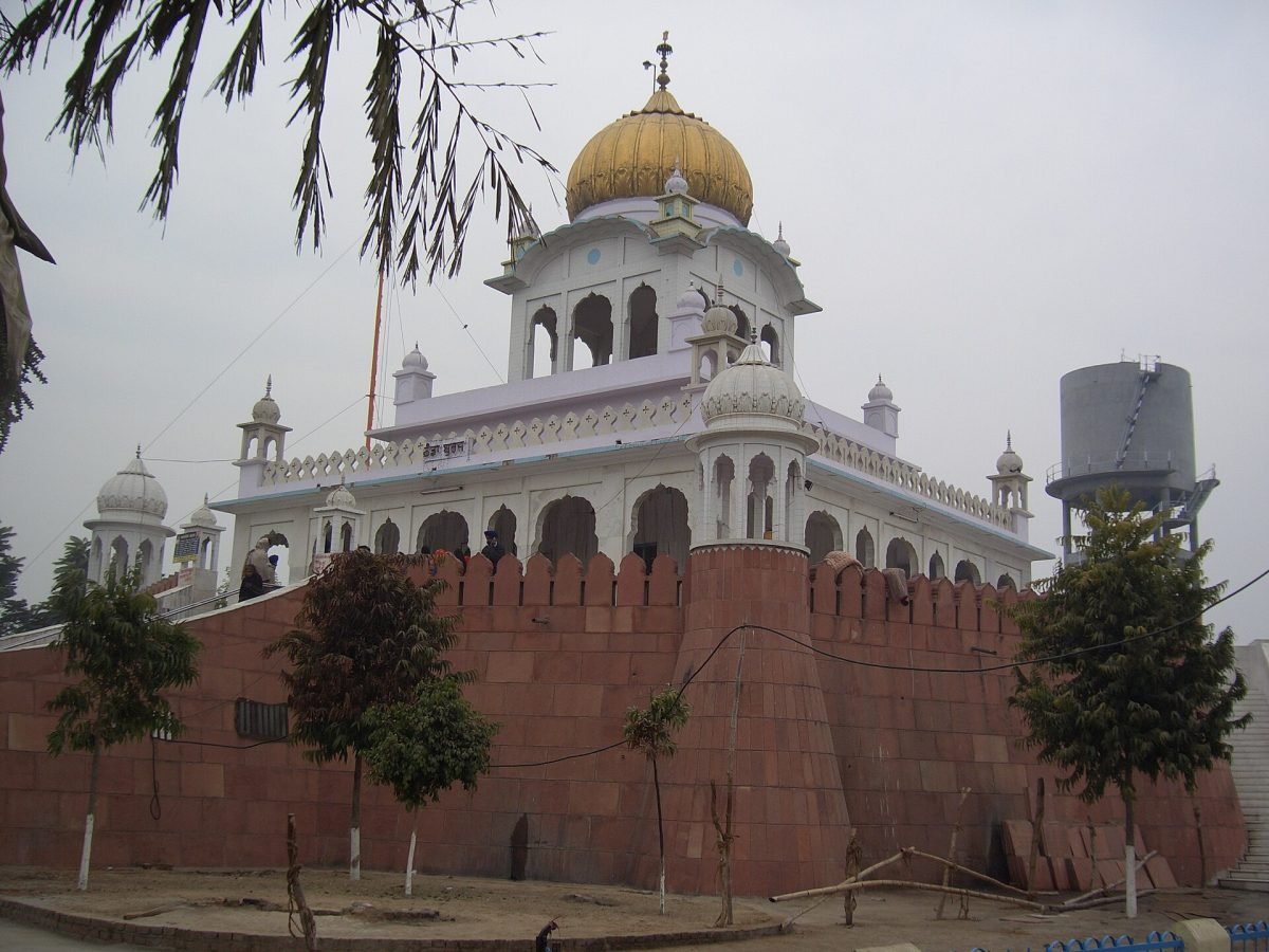 A white gurdwara with a golden dome rising above a high red sandstone wall