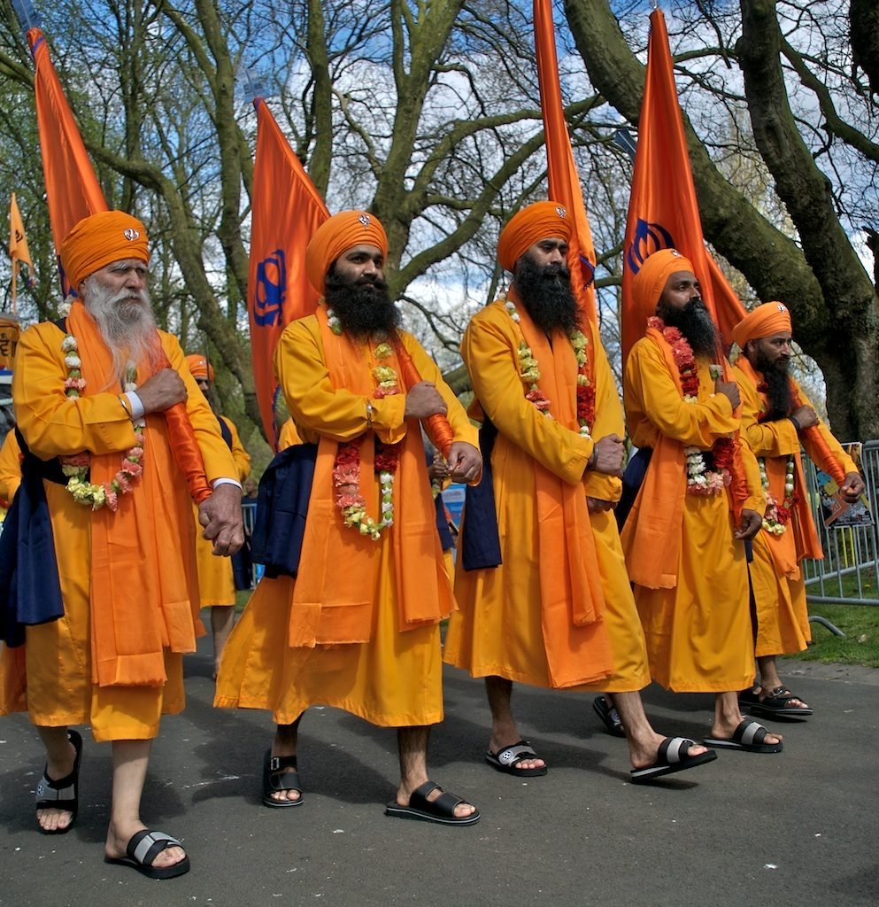 Five Sikh men in saffron robes walking in a street procession