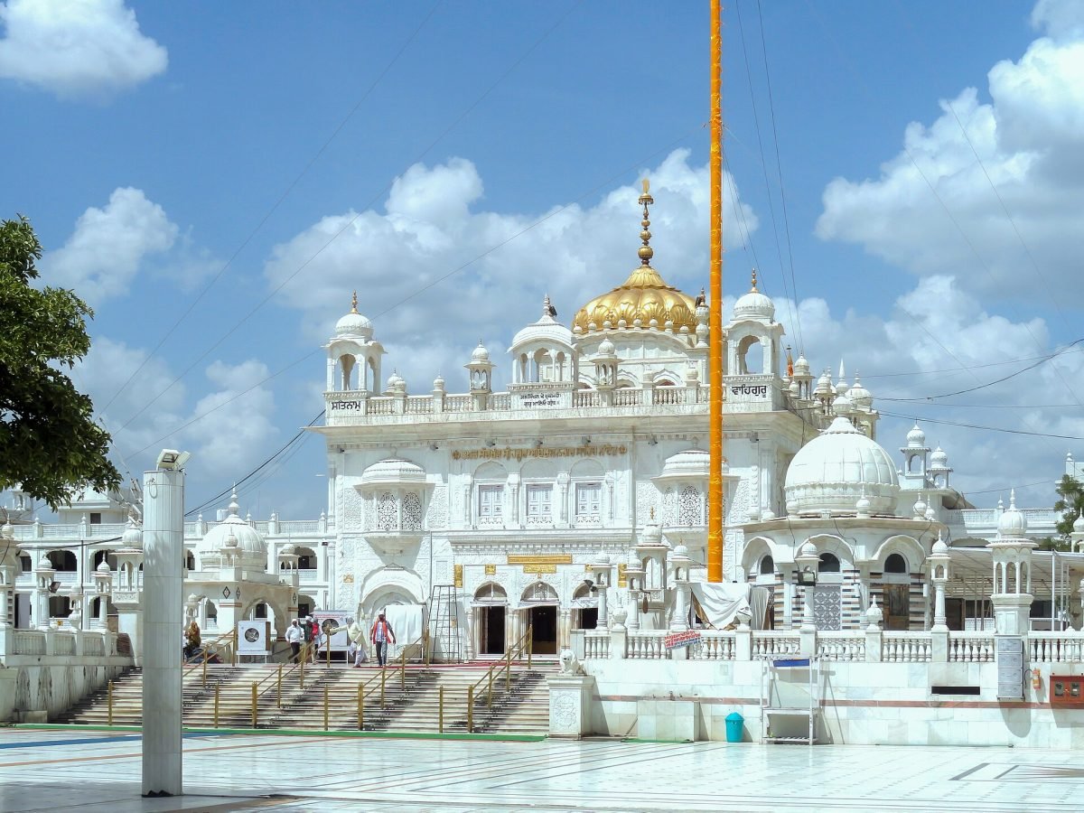 A white gurdwara with a golden dome against a blue sky, with a paved courtyard in front