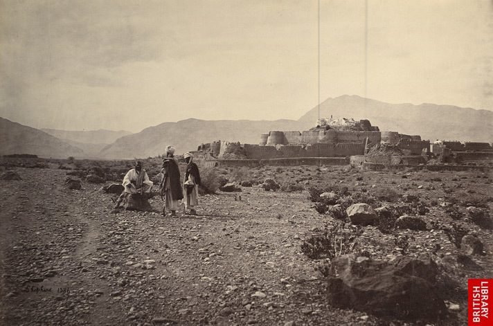 A black and white photograph of a high-walled fort on a rise, with bare hills behind it