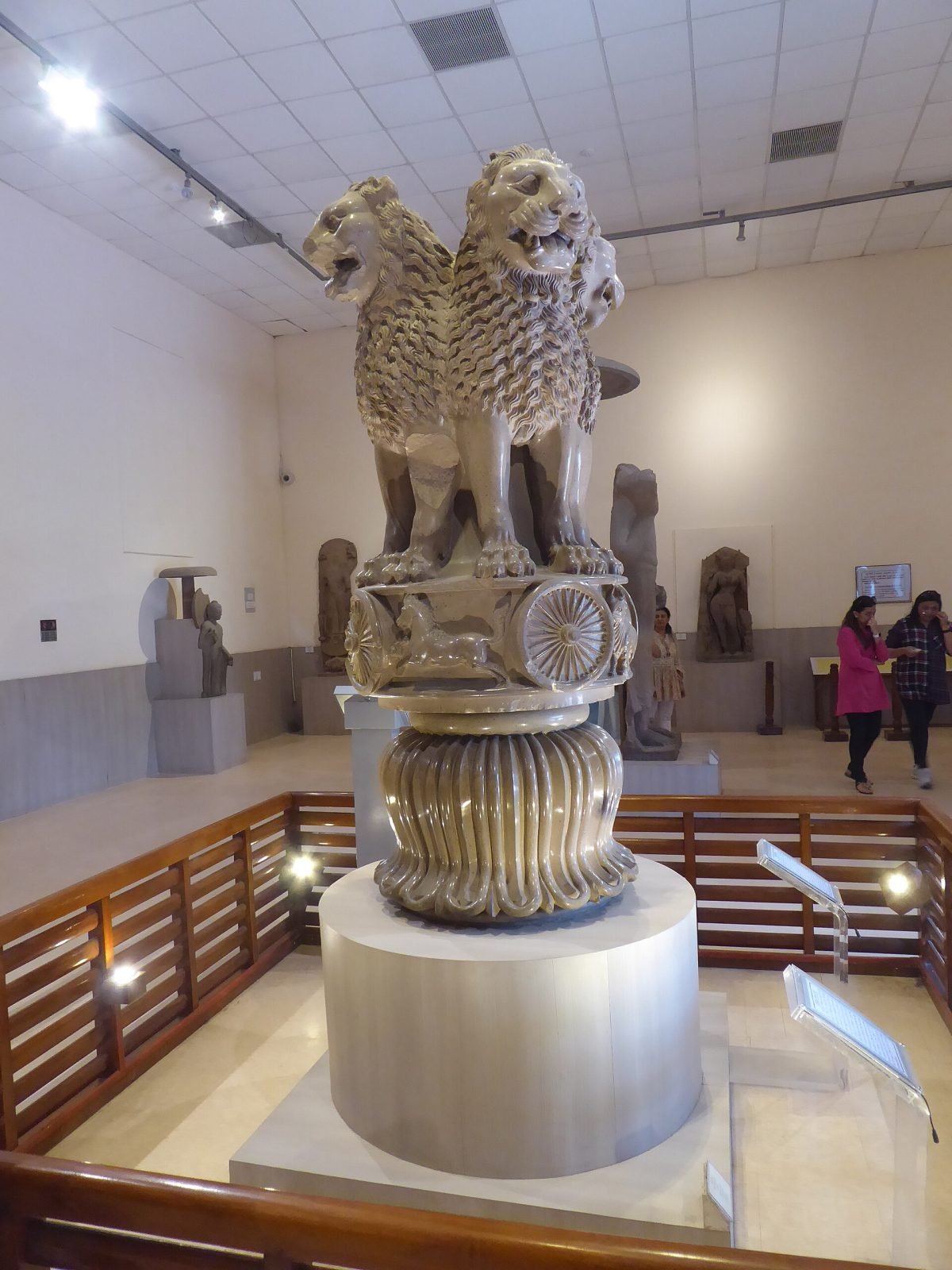 A polished stone sculpture of four lions seated back to back on a round base carved with animals and wheels, displayed in a museum