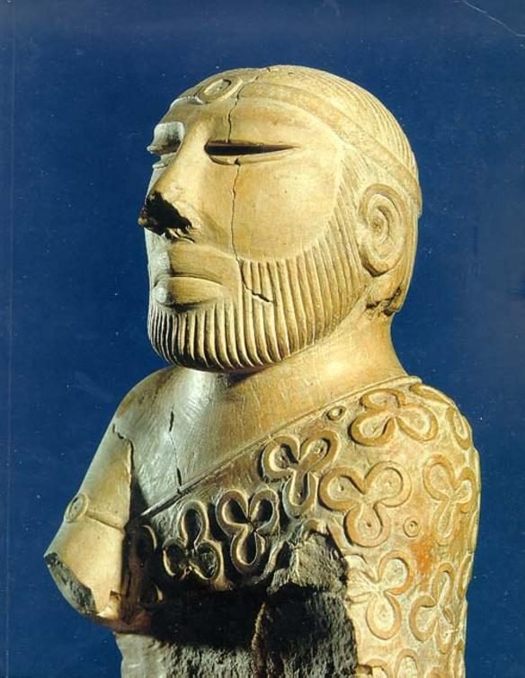 A small carved stone bust of a bearded man with a headband and a robe patterned with trefoils