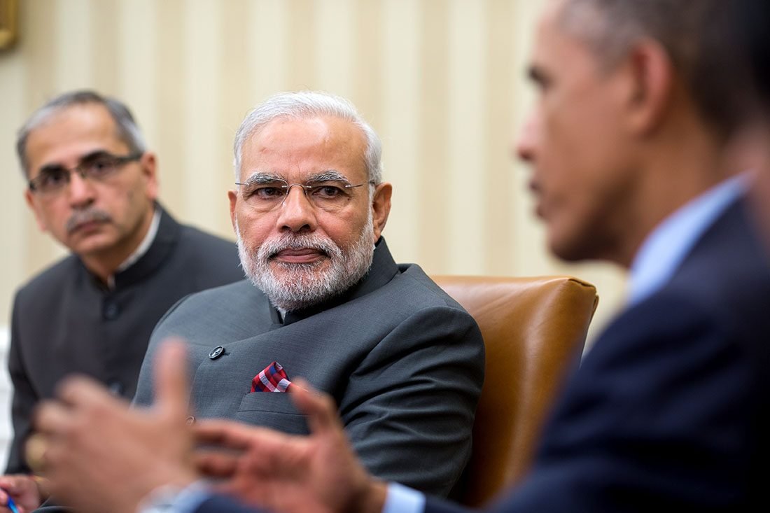Barack Obama and Narendra Modi seated in armchairs talking in the Oval Office
