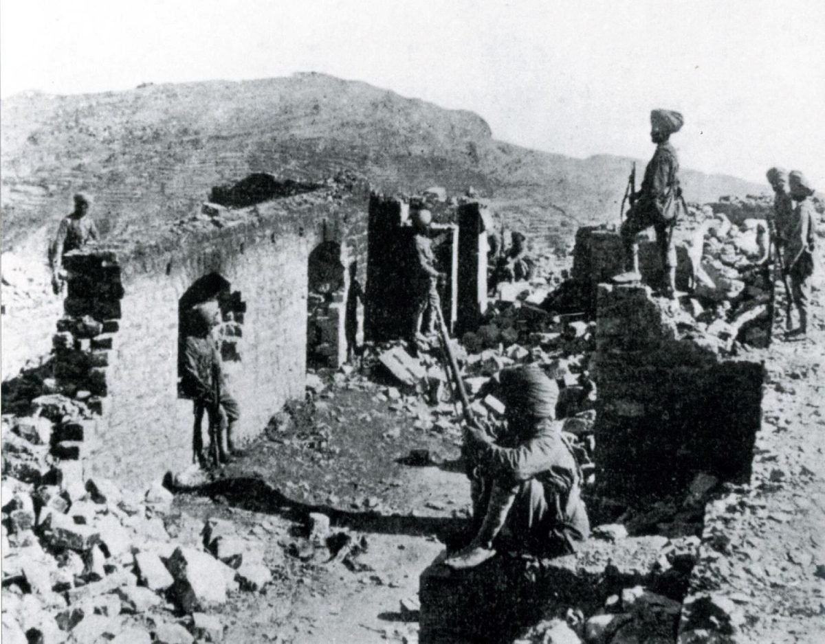 An old photograph of the burnt-out stone ruins of a hilltop post, with a fort on the distant skyline