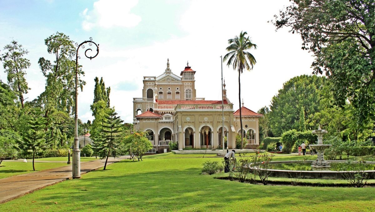 A wide cream-coloured palace with arched verandas and a lawn in front, in Pune
