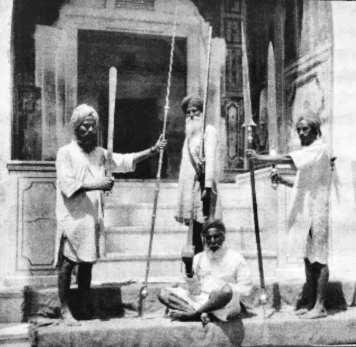 Four turbaned men hold up old guns, spears and swords