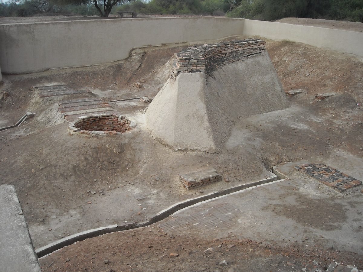 A round brick-lined well beside flat brick platforms in an excavated area of ancient ruins